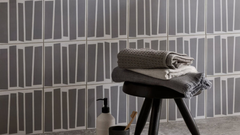 Stack of folded textured gray and white towels resting on a black stool in black and white wall tiles collection