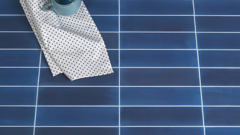 A light blue ceramic mug with a glossy finish sits on a white cloth with black stars in the blue floor tiles collection