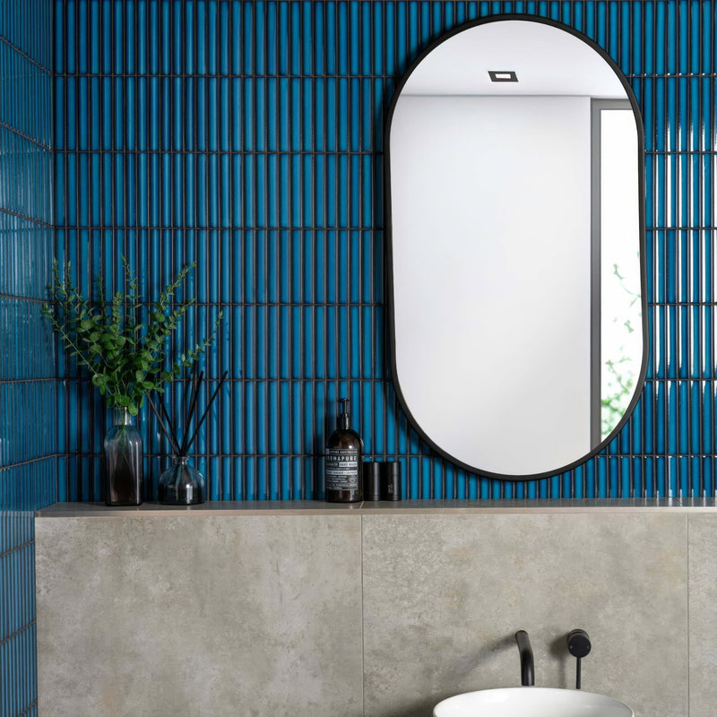 Oval-shaped mirror with sleek black frame mounted on a vibrant blue mosaic tiled wall for stylish decor.
