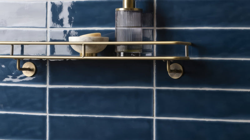 Gold-toned metal shelf with sleek minimalist design mounted on blue brick wall tiles in modern interior setting