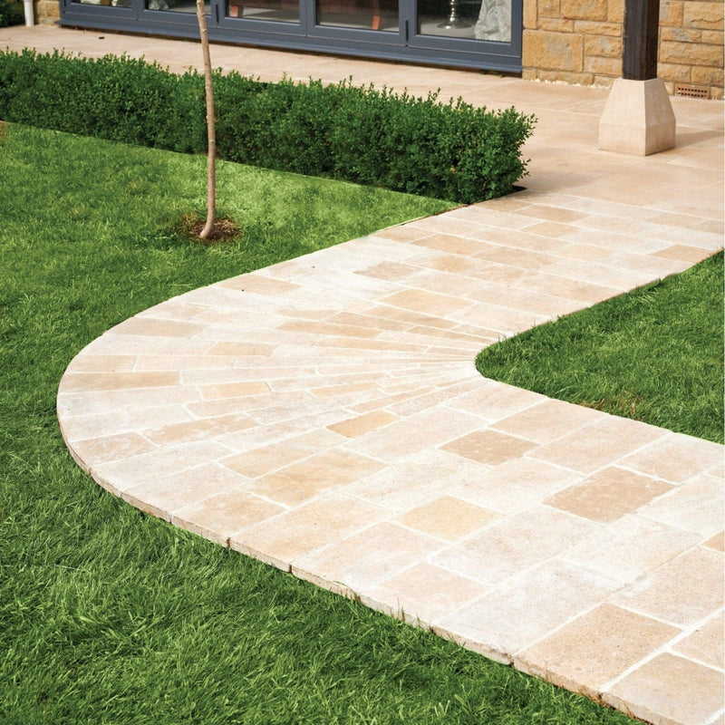 A curved pathway made of light beige buscot limestone pavers laid between vibrant green grass