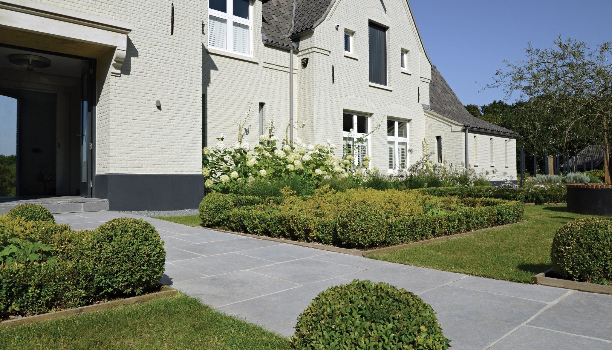 A modern light beige brick house with dark gray accents and white-framed windows featuring ca’ pietra outdoor stone and porcelain tiles