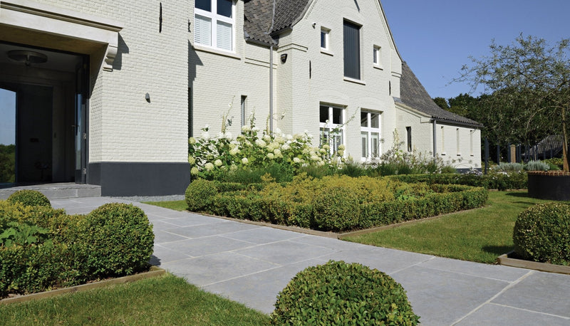 A modern light beige brick house with dark gray accents and white-framed windows featuring ca’ pietra outdoor stone and porcelain tiles