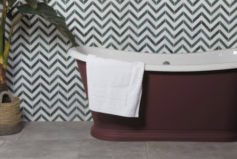 Maroon freestanding bathtub with white rim and towel in Ca’Pietra Decorative Stone and Tiles collection