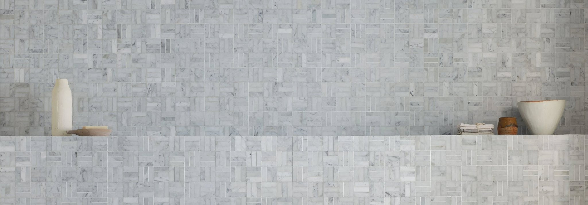 The wall features light gray carrara marble tiles with subtle veining arranged in an interlocking mosaic pattern