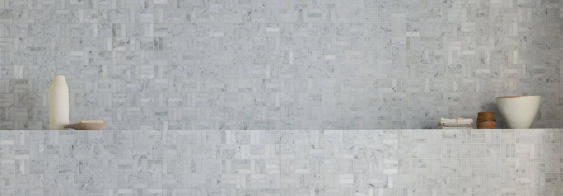 The wall features light gray carrara marble tiles with subtle veining arranged in an interlocking mosaic pattern