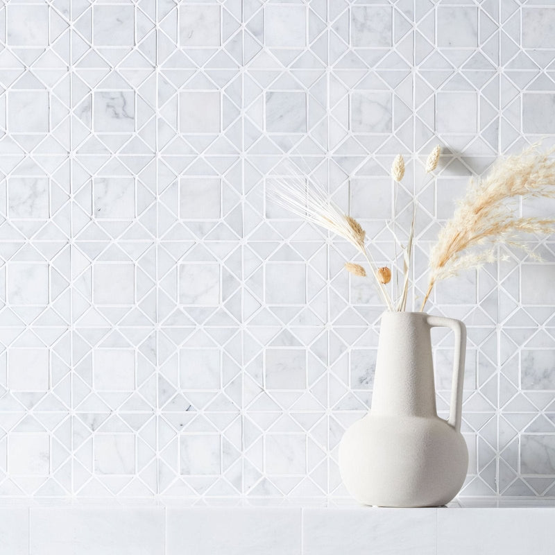 A matte white ceramic pitcher with a rounded body and handle holding dried pampas grass in carrara white marble tiles