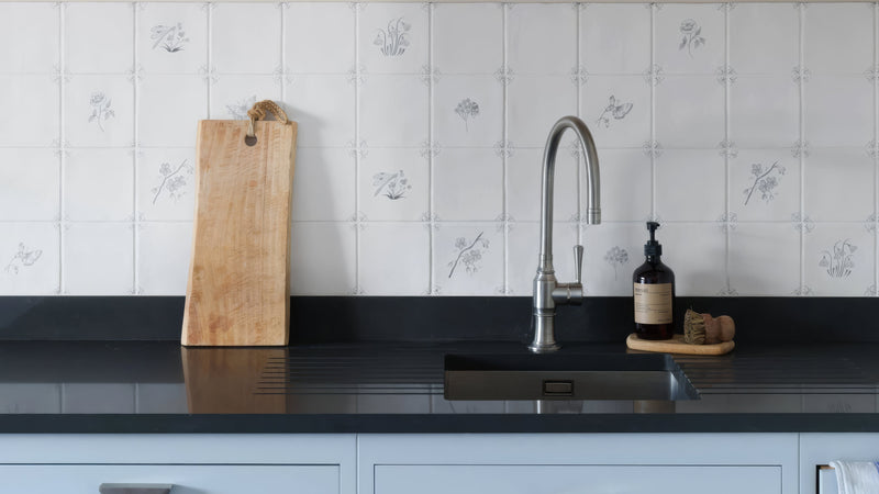 A sleek modern stainless steel kitchen faucet with a curved spout and single lever handle in ceramic kitchen tiles.