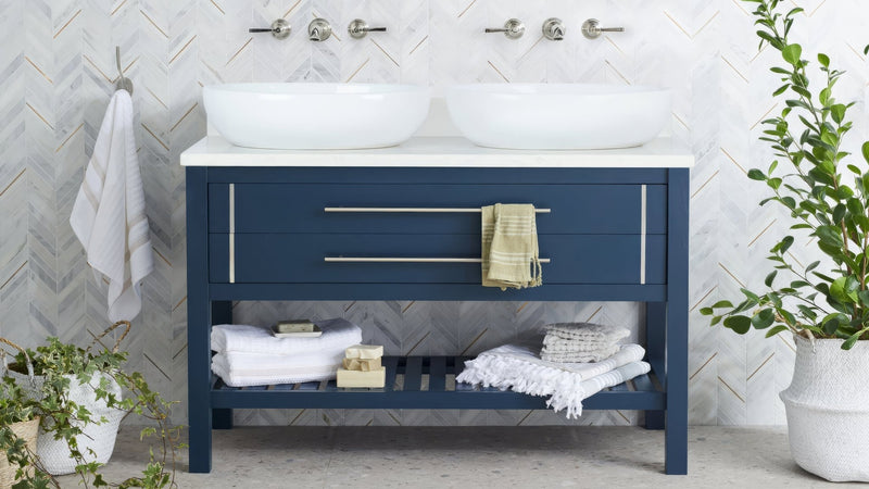 Navy blue bathroom vanity with two white ceramic sinks and silver hardware in a chevron bathroom tiles collection.