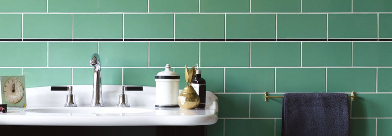 A bathroom sink with a white ceramic basin and chrome faucet against green subway tiles in the cinema collection