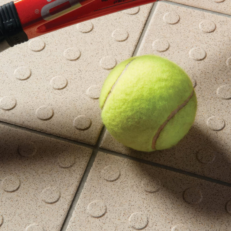A bright yellow tennis ball with fuzzy texture and brown seams resting on textured beige dorset woolliscroft multidisc tiles