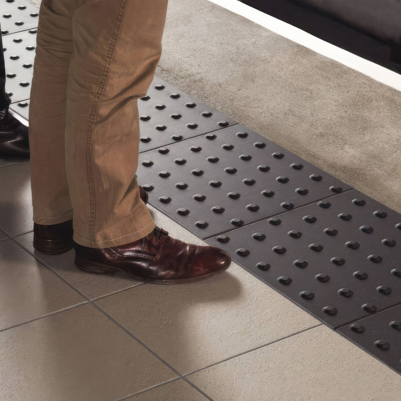 Black textured Dorset Woolliscroft tactile blister paving tiles with raised circular bumps for accessibility guidance