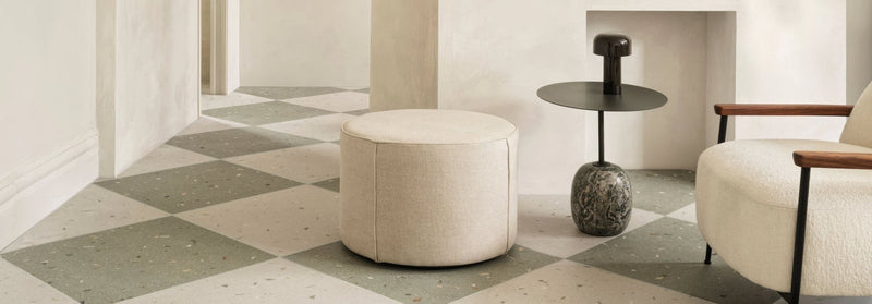 Cream-colored cylindrical pouf with soft textured fabric upholstery from the fired earth floor tiles collection.