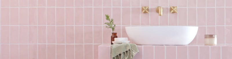 White oval sink with gold faucet fixtures against pink tiled wall from forecast tiles collection