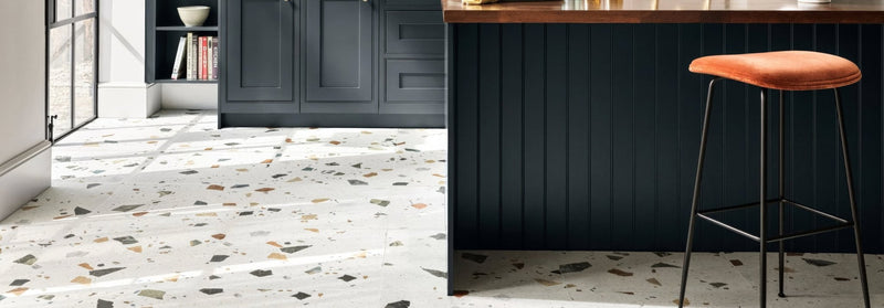 Terrazzo floor tile with a white base and scattered black gray and earthy brown chips from frammentio tiles collection