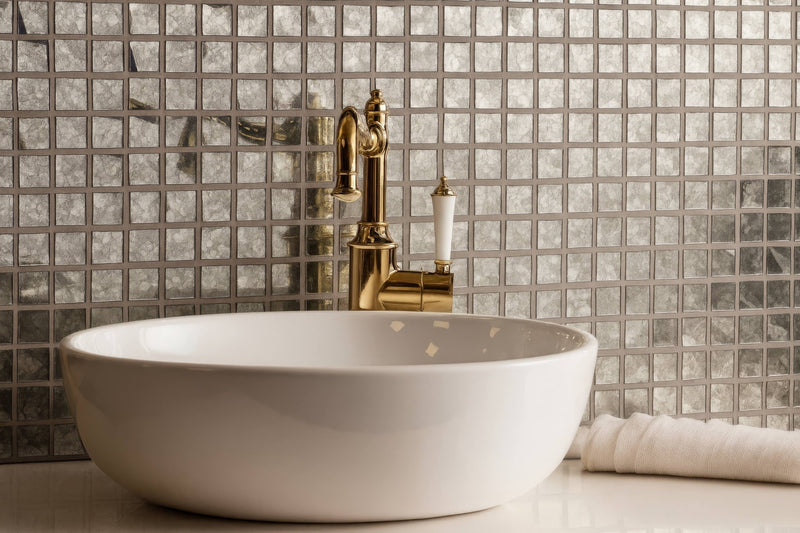 White ceramic vessel sink with polished gold faucet displayed with glass mosaic tiles background