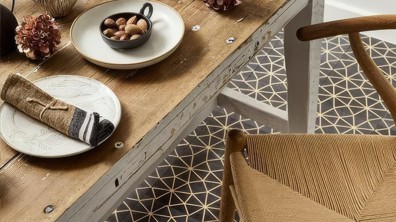 A rustic wooden table with a weathered white finish holding a bowl of nuts and a rolled napkin in gold floor tiles collection