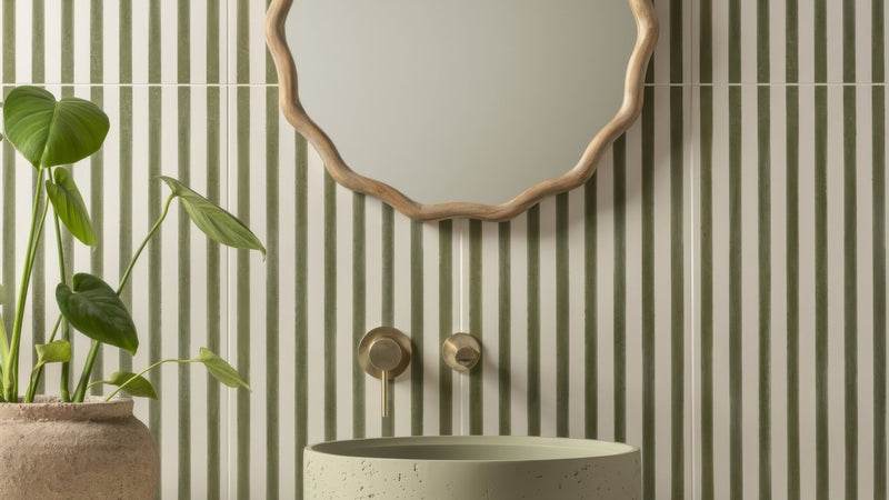 A round light green concrete sink with speckled texture under modern gold toned faucets in green wall tiles collection