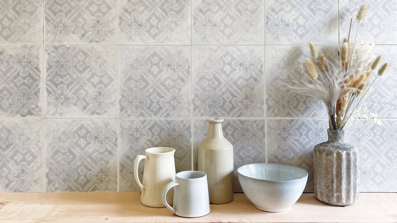 A collection of ceramic tableware in soft neutral tones with subtle textured surfaces including pitcher mugs and bowl.