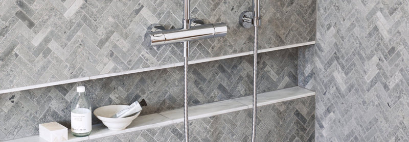 Chrome-finished shower faucet with sleek modern design mounted on gray herringbone stone tile from Hampton Bays Tile Collection