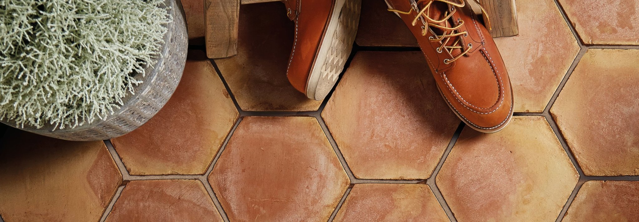A pair of tan leather work boots with brown laces on hexagonal handmade classic terracotta tiles