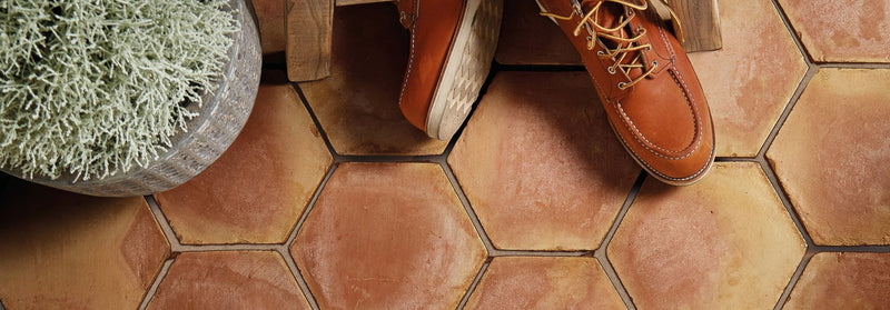 A pair of tan leather work boots with brown laces on hexagonal handmade classic terracotta tiles