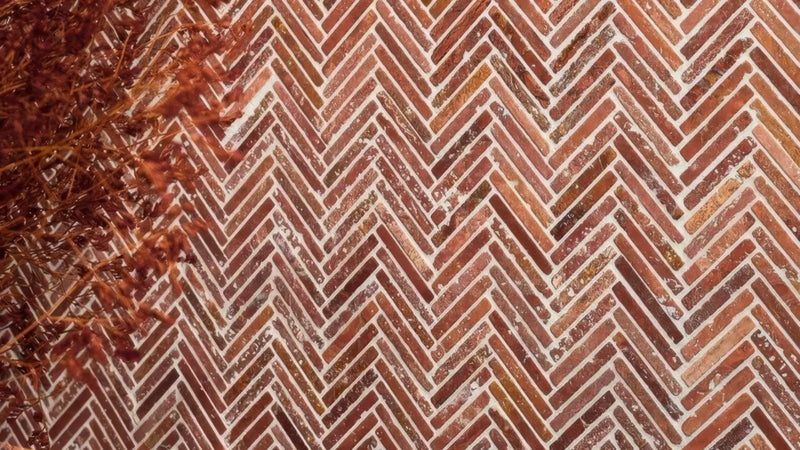 Reddish-brown brick herringbone mosaic tiles with white mortar showcasing a classic interlocking pattern.