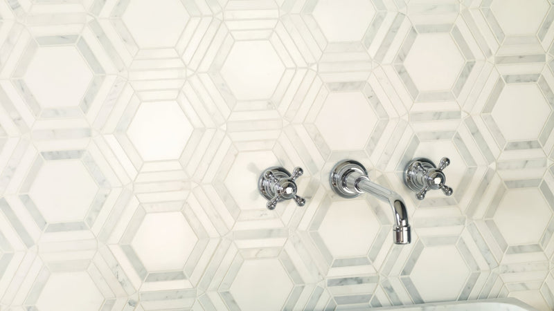 Chrome-finished wall-mounted faucet with two cross handles and curved spout against white hexagonal marble tiles