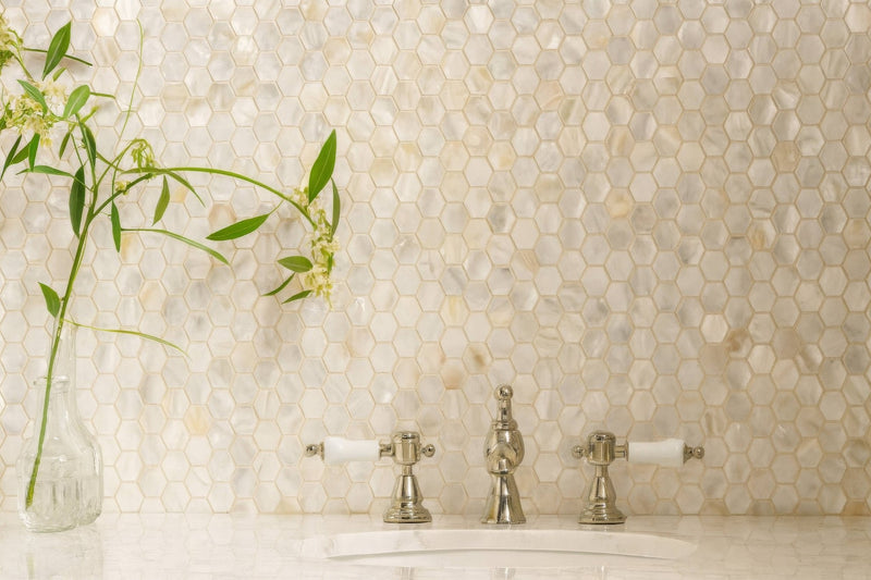 Shiny silver faucet with white ceramic handles against iridescent mother-of-pearl hexagon mosaic tiles backdrop