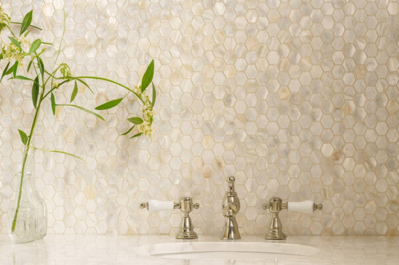 Shiny silver faucet with white ceramic handles against iridescent mother-of-pearl hexagon mosaic tiles backdrop