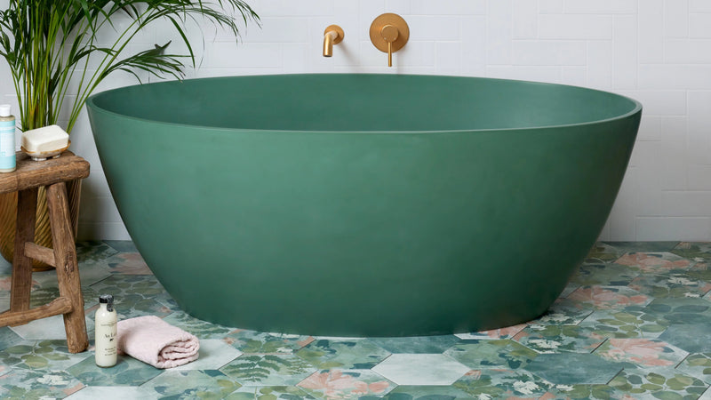 A sleek matte green freestanding oval bathtub with gold fixtures in a modern hexagon tiles collection