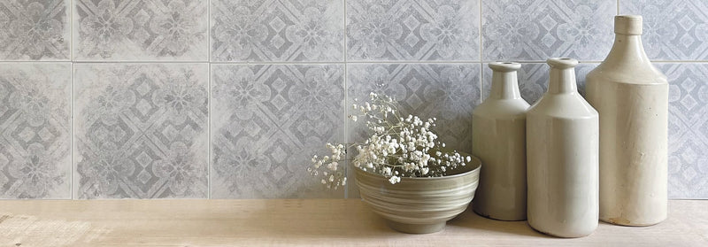 A set of three matte off-white ceramic bottles with slender necks beside a ribbed bowl holding white baby’s breath in istria tile collection