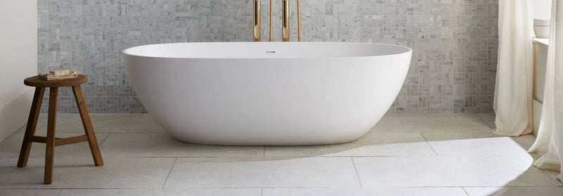 A sleek white freestanding porcelain bathtub with oval design and minimalist gold fixtures from Jerusalem porcelain tile collection