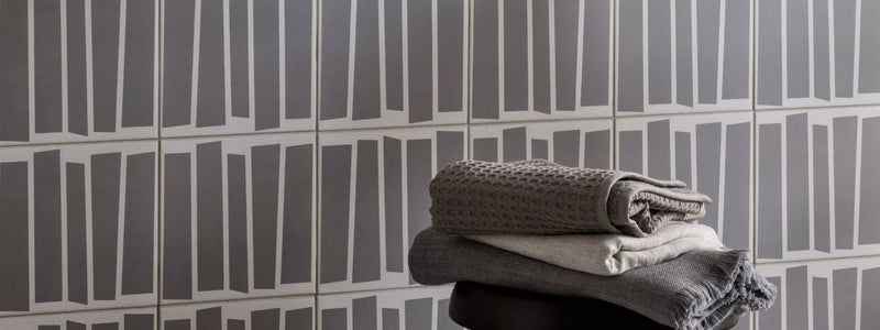 Stack of folded gray and white textured towels from the Kelly Hoppen Tile Collection with a soft fabric finish.