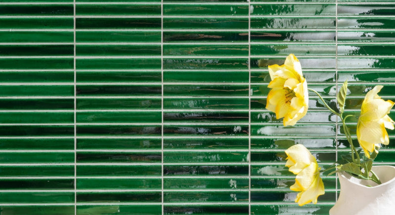 A white ceramic vase holding yellow flowers against glossy green rectangular tiles from the koeda mosaic collection