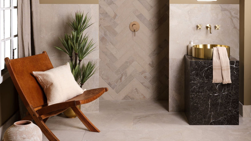 Gold bowl sink with black marble pedestal displayed against a limestone wall tile background