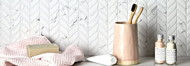 Pink ceramic toothbrush holder with gold base holding two wooden bamboo toothbrushes displayed with malmo recycled glass tiles