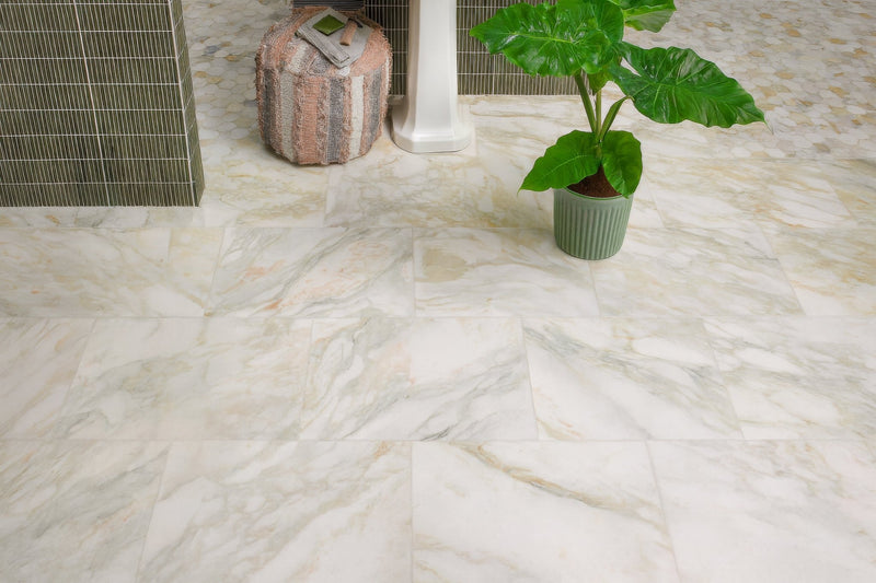 A potted plant with broad green leaves in a textured sage green ceramic pot displayed with marble bathroom tiles