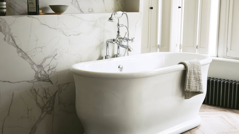White freestanding bathtub with classic curved design and chrome faucet fixtures in marble effect bathroom tiles collection
