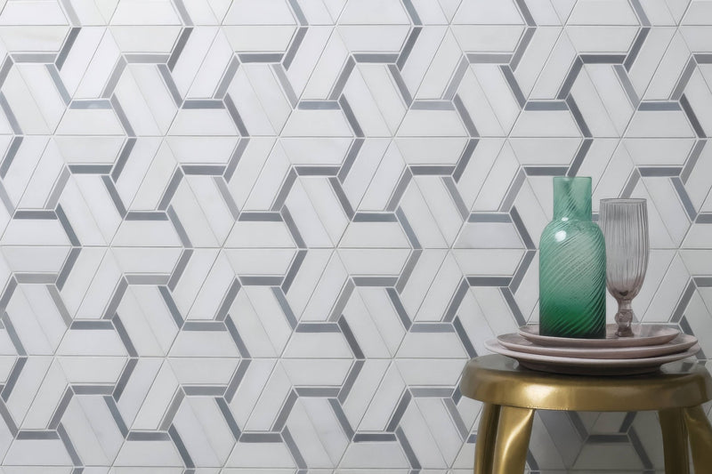A translucent teal glass vase with a ribbed texture on stacked plates atop a gold stool in marble mosaic tiles collection.