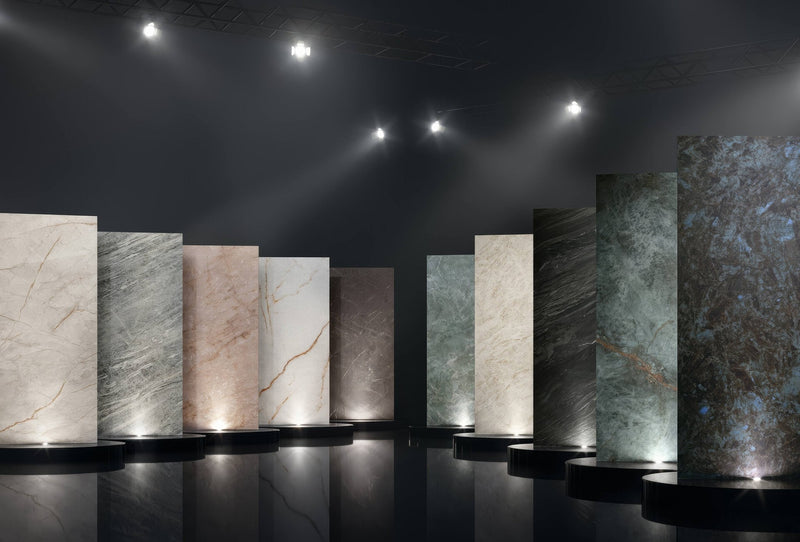 Rows of polished marble slabs in earthy tones with natural veining on black pedestals from marvel diva tile collection