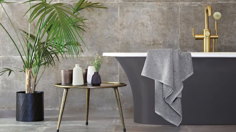Gold-toned metal side table with slender legs and round top holding decorative vases in metal effect bathroom tiles collection
