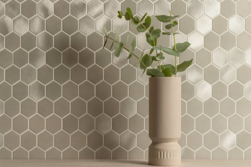 Beige ceramic vase with fluted base and smooth body holding fresh eucalyptus branches in metal mosaic tiles collection