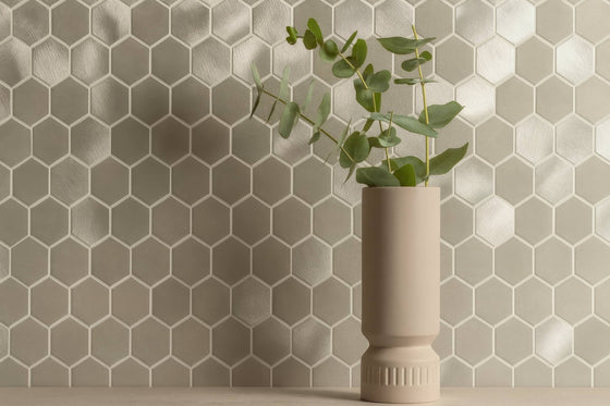 Beige ceramic vase with fluted base and smooth body holding fresh eucalyptus branches in metal mosaic tiles collection