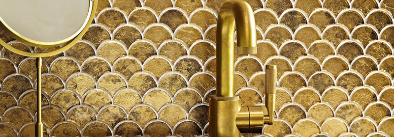 Gold-toned sleek faucet with curved spout and minimalist design against gold fish-scale mosaic tile backsplash from metallic vitreum mosaic collection