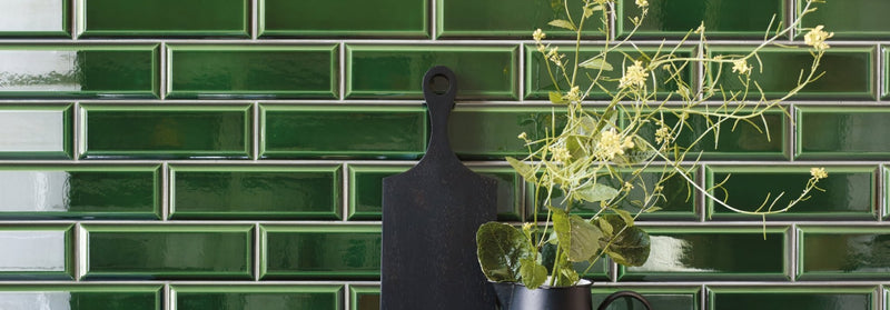 Black cutting board with handle made of durable material against glossy green subway tiles from metropolitan tile collection