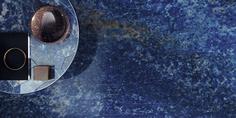 A glossy deep brown spherical bowl with a speckled metallic finish on a circular mosaic tray from minoli marble look tiles