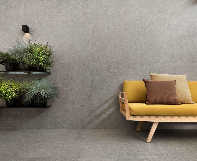 Yellow upholstered sofa with wooden frame and two throw pillows in a minoli stone look tiles setting