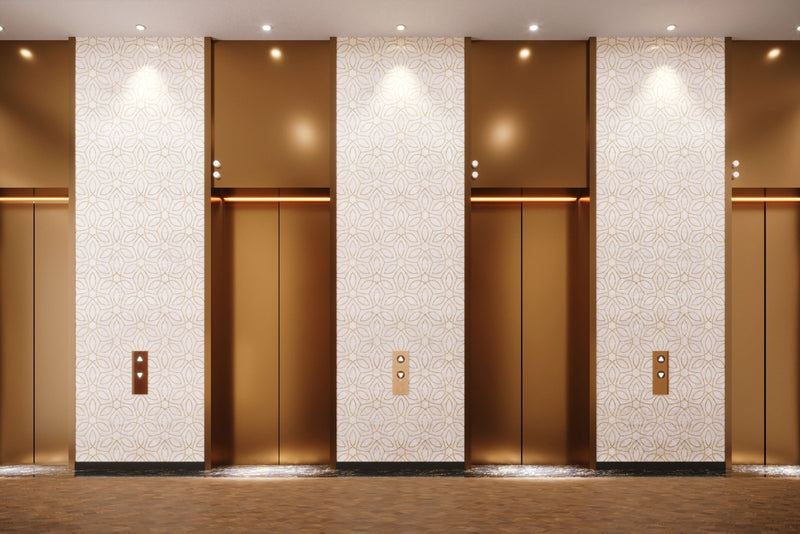 Gold-finished elevator doors with a sleek modern design and subtle embossed mother of pearl wall panels surrounding them