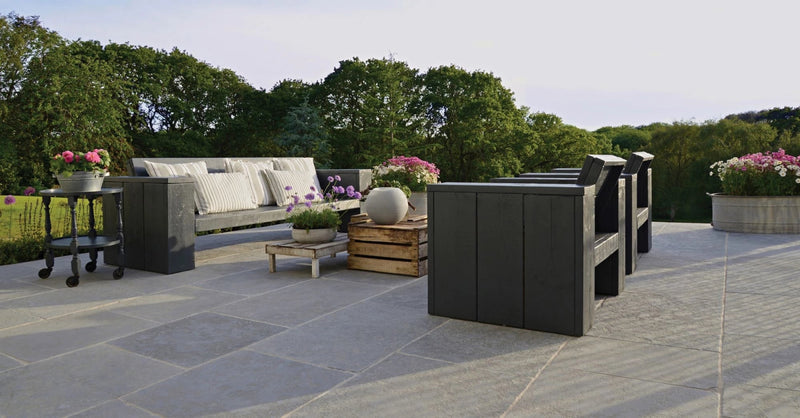 Modern dark gray outdoor sectional sofa with white striped cushions and wooden crate side tables on natural stone paving tiles